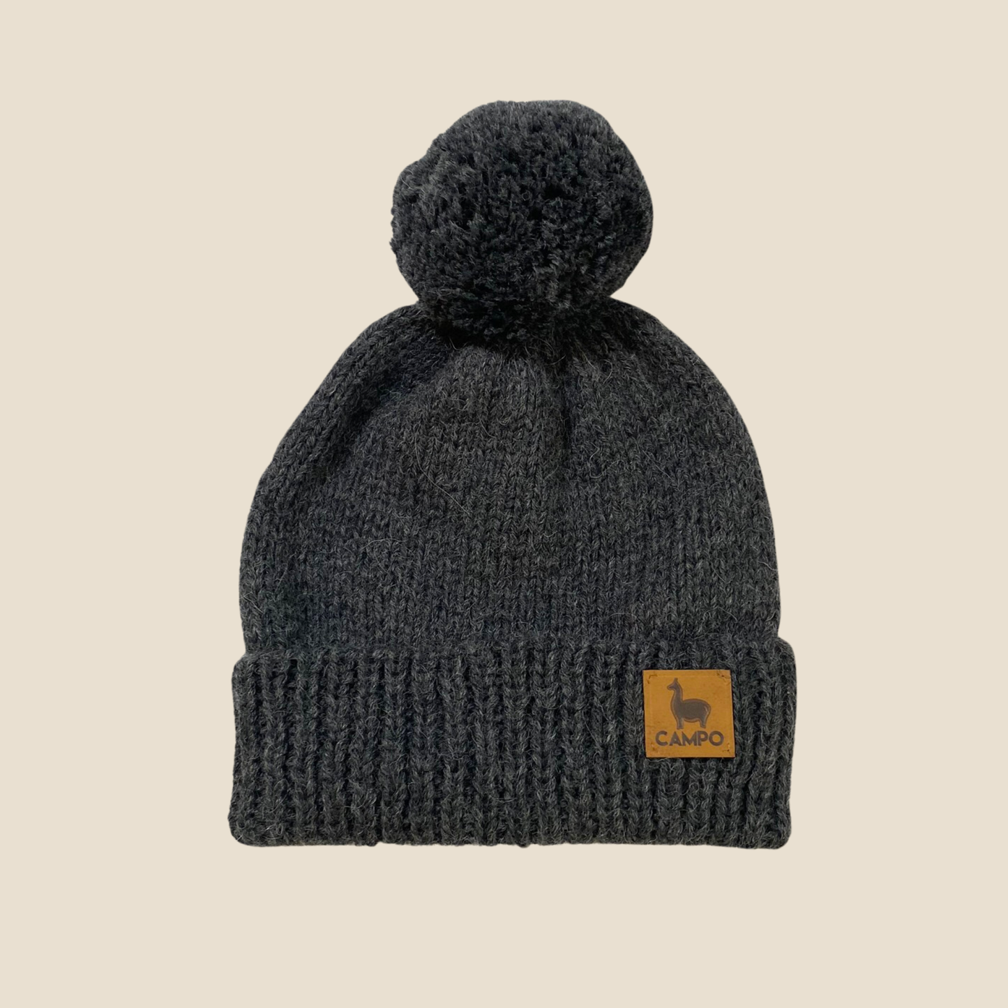 Dark gray knit beanie with a pom-pom on a beige background, featuring a 'Campo' label.