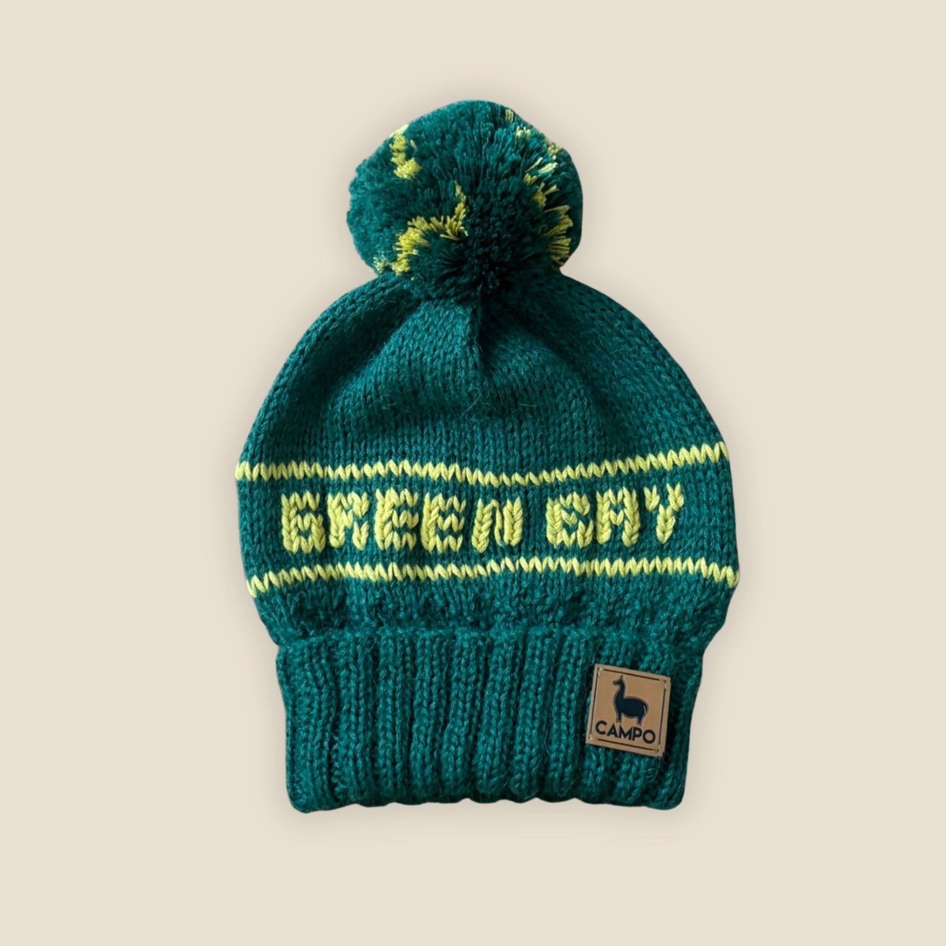 green knit beanie with yellow text and a pom-pom on a beige background