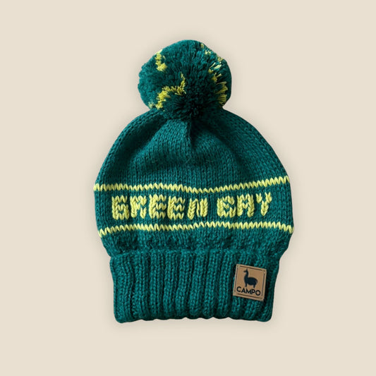 green knit beanie with yellow text and a pom-pom on a beige background