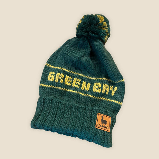 Green knit beanie with yellow text and a logo on a beige background