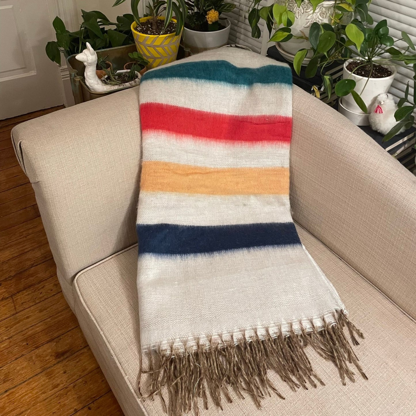 Colorful striped blanket draped over a beige couch in a living room setting with plants.