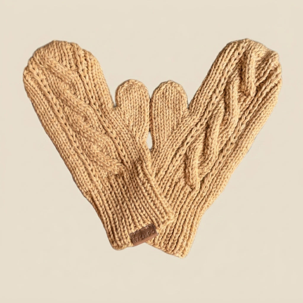 A pair of chunky cable-knit mittens in a warm camel tan color, arranged overlapping on a solid light beige background.
