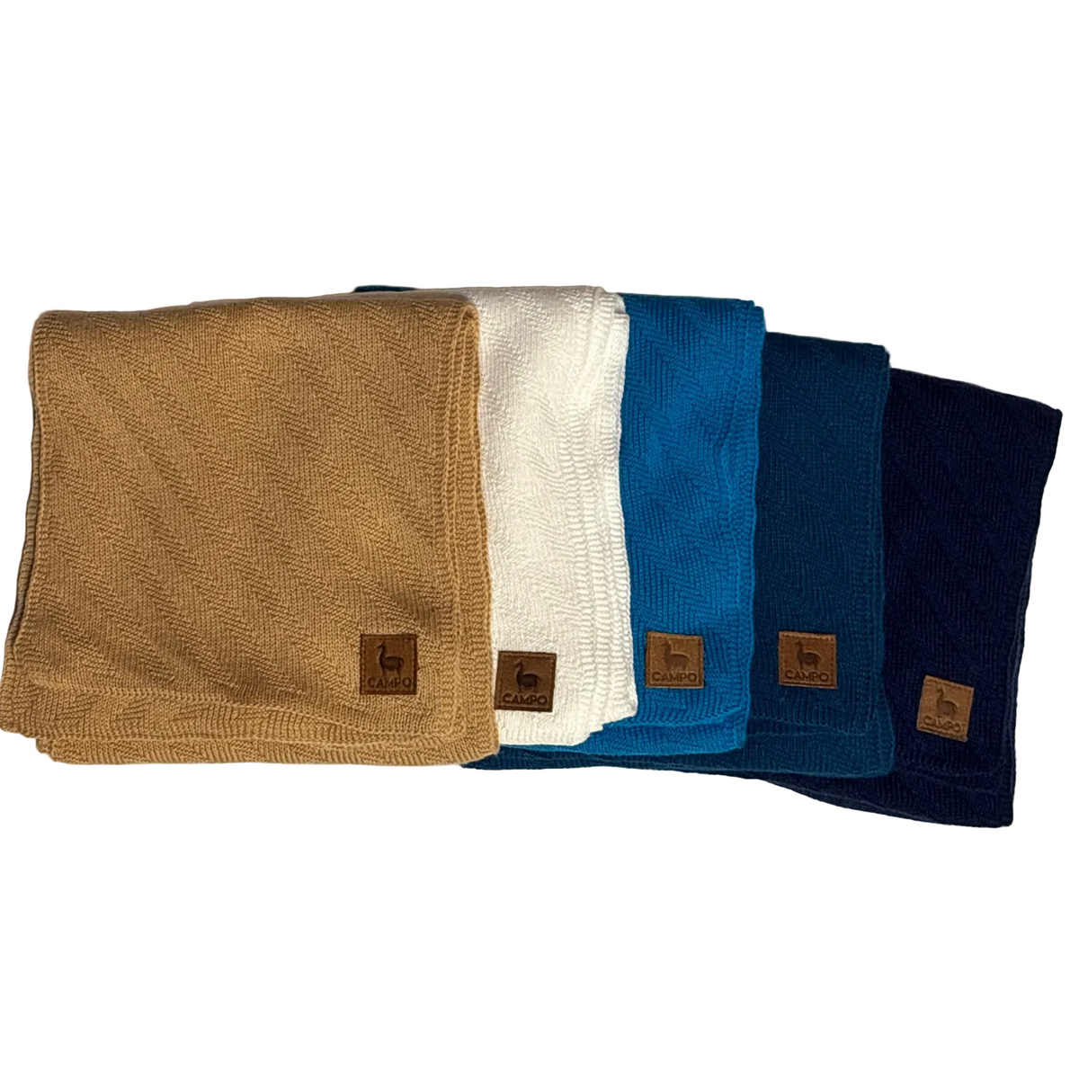 Four folded ribbed knit neck warmers or beanies in tan, off-white, bright blue, and navy, arranged in a row on a light surface with a soft shadow. Each has a small brown leather patch with a deer logo and the brand name 'b&cabin'.