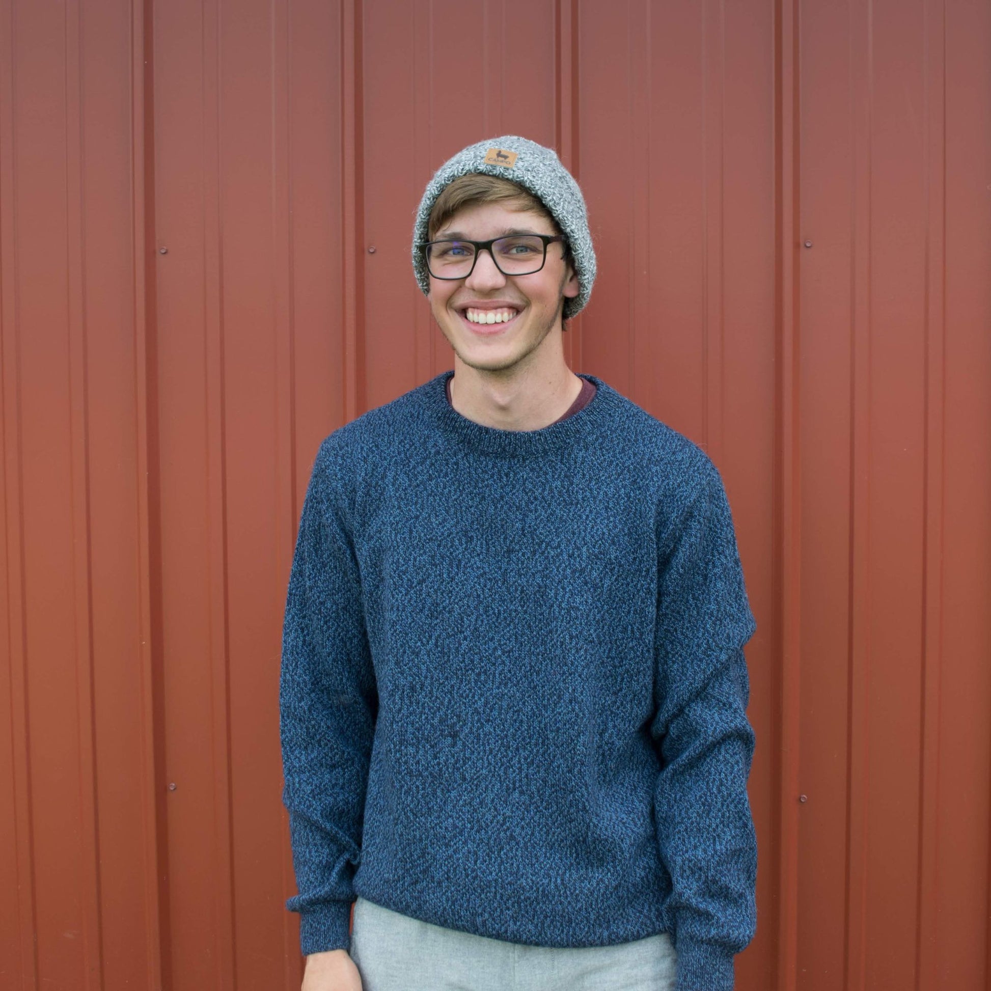 Person wearing a blue sweater and gray beanie standing in front of a red wall