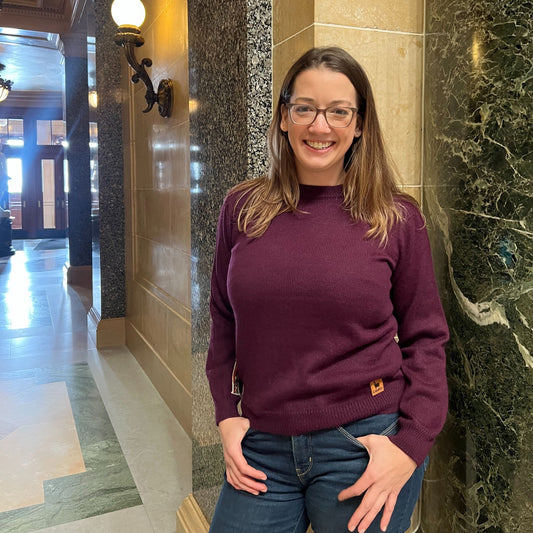 Woman wearing a purple sweater and glasses standing in a marble hallway
