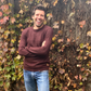 Man in a maroon sweater standing in front of a leafy wall