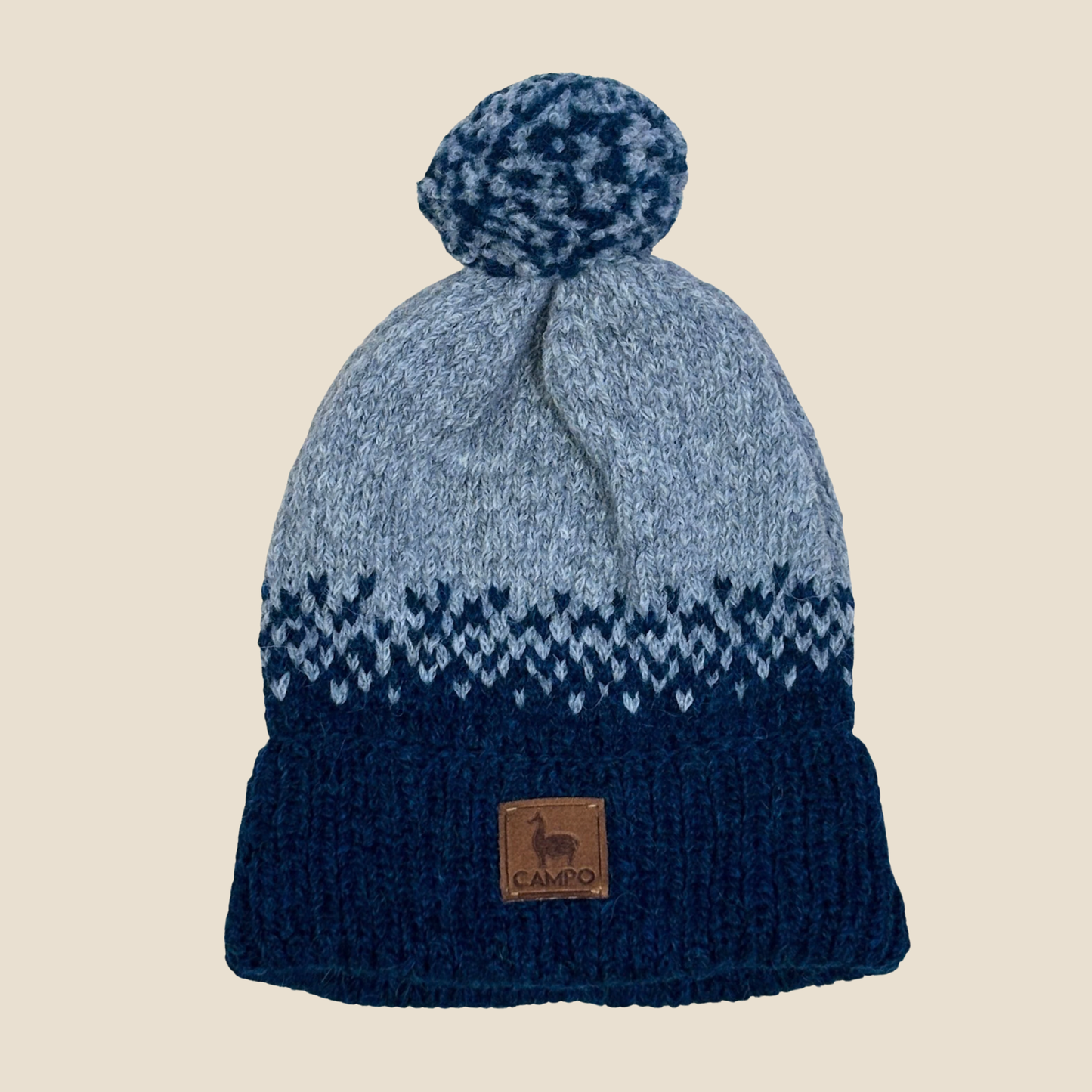 Blue and gray knit beanie with a pom-pom on a beige background