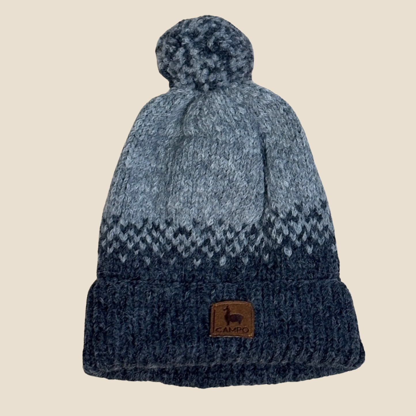 Blue knit beanie with a pom-pom on a beige background