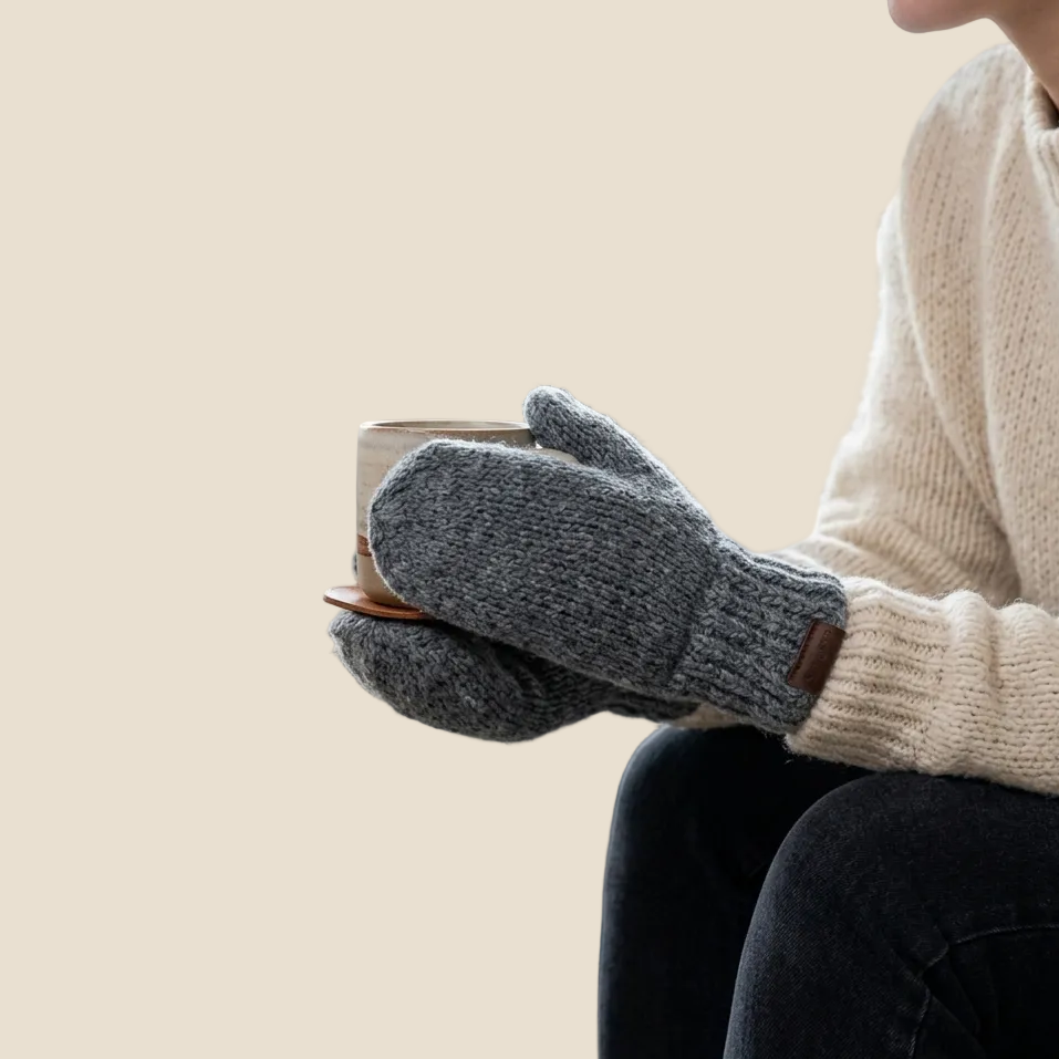 Person wearing gray gloves holding a mug in a cozy indoor setting