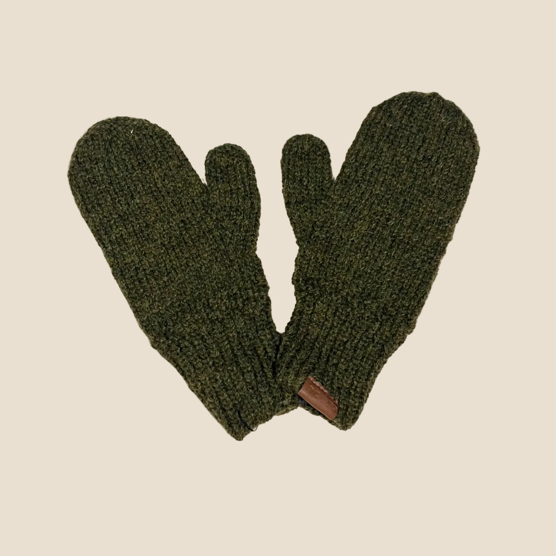 A pair of dark olive green knit mittens with a small brown leather brand tab, displayed against a solid cream background.