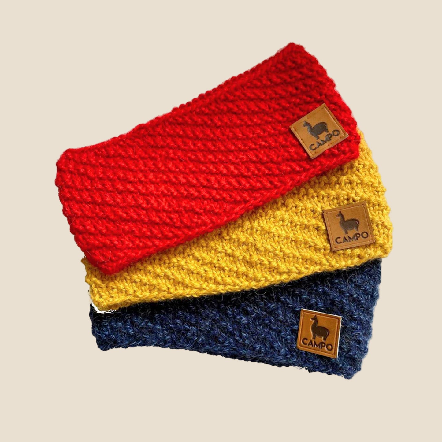 Three knitted scarves in red, yellow, and blue with 'Camilo' brand labels on a white background.