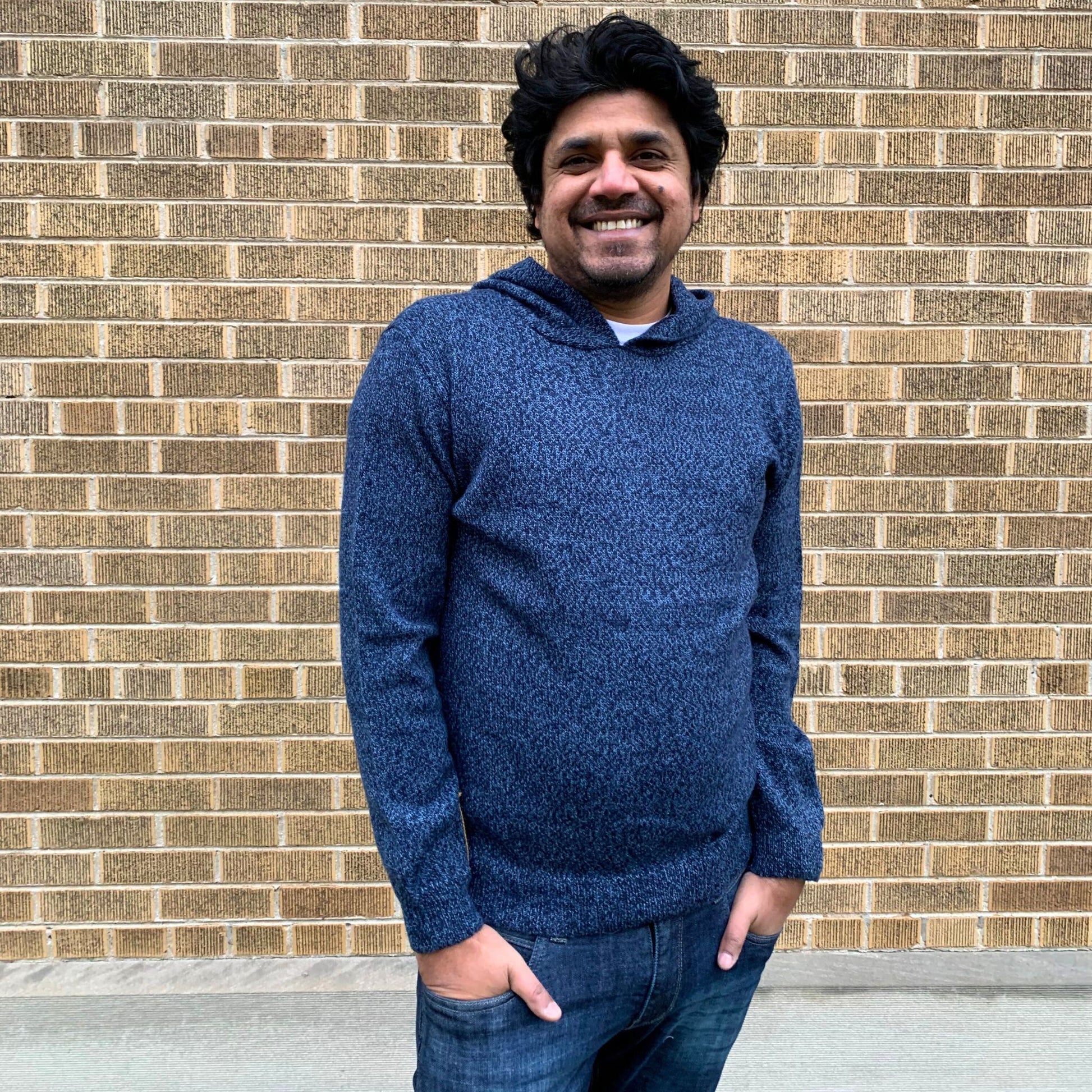 Man wearing a blue hoodie standing in front of a brick wall