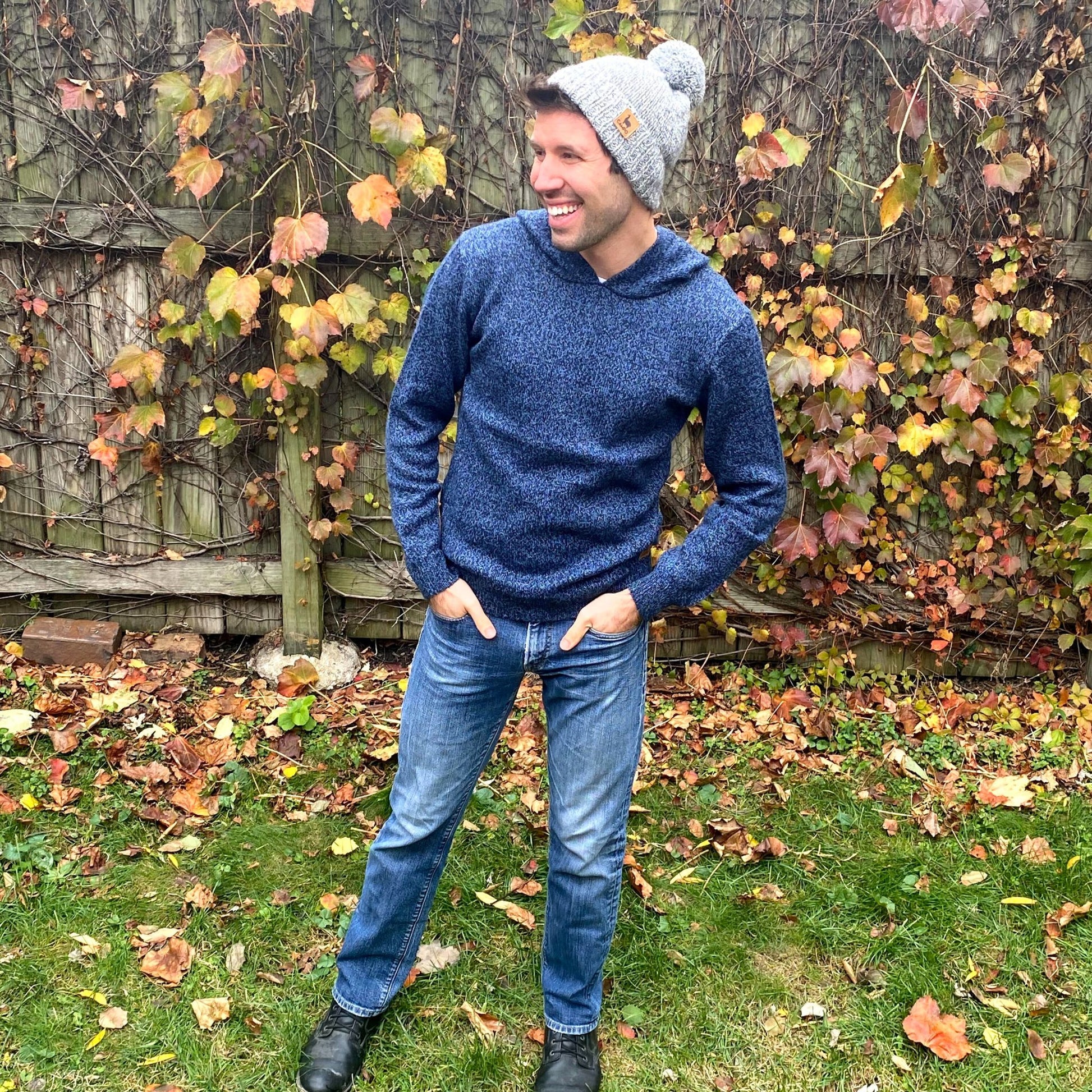 Man wearing a blue hoodie and gray beanie standing in an autumn garden.