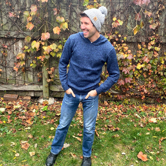 Man wearing a blue hoodie and gray beanie standing in an autumn garden.