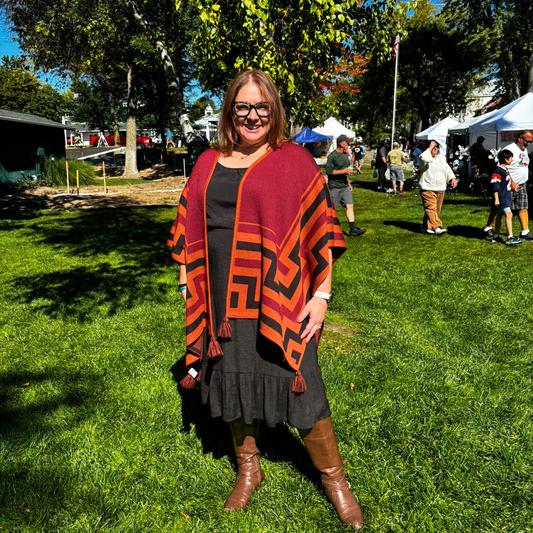 Woman wearing a colorful Alpaca Shawls standing on grass with people and tents in the background