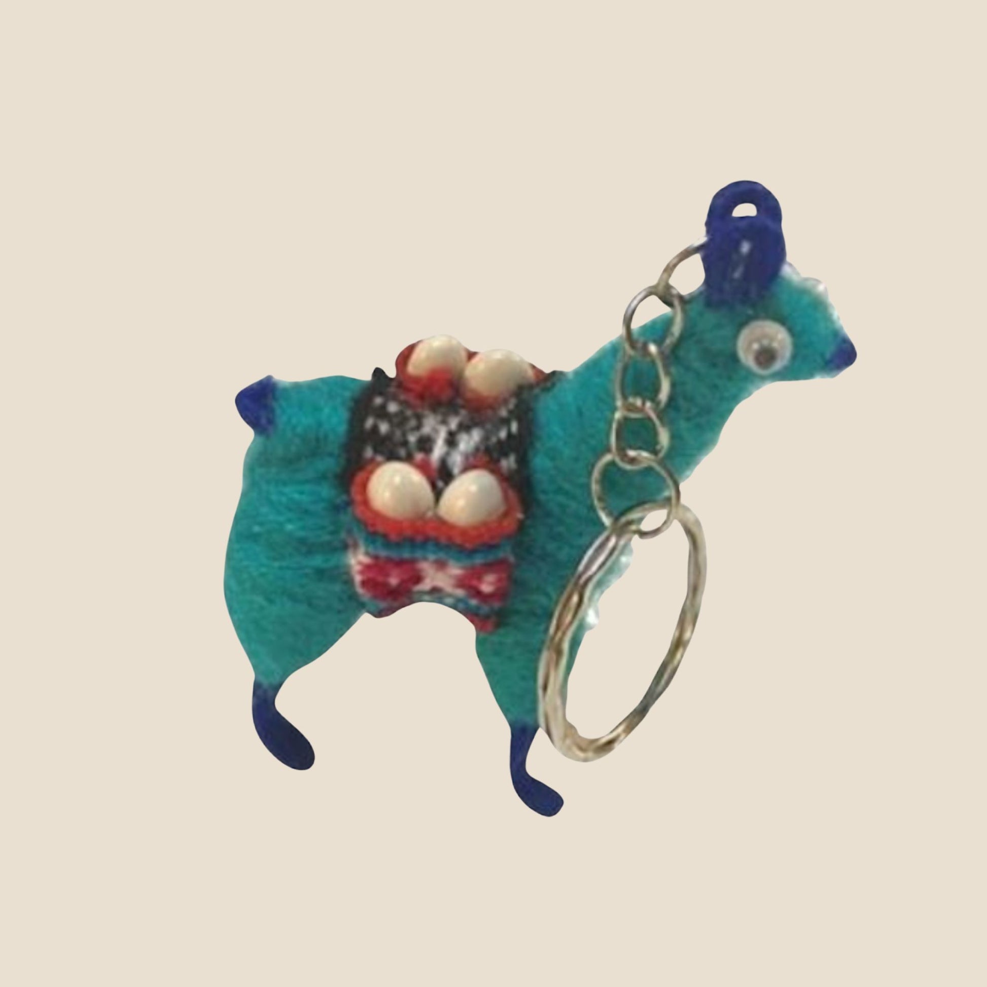 Blue alpaca-shaped keychain with a colorful sweater on a beige background
