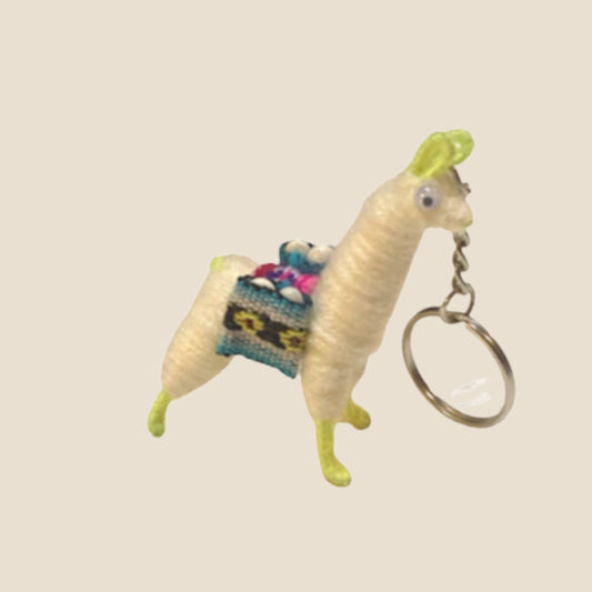 Alpaca shaped keychain with a colorful saddle on a beige background