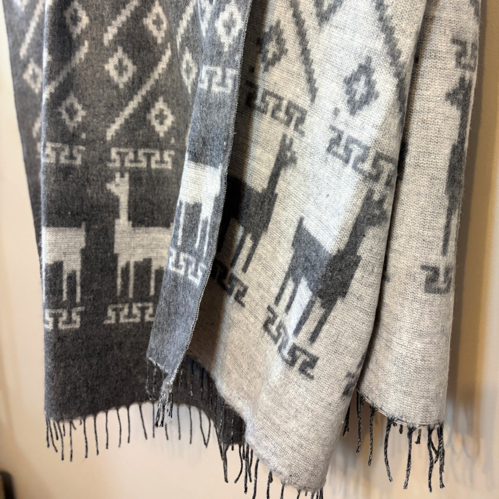 Textile with alpaca pattern and fringe details on a plain background