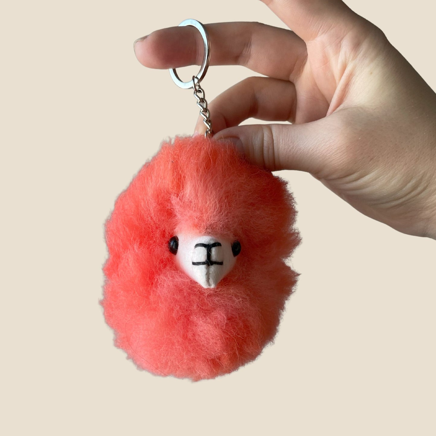 Hand holding a red fluffy keychain with a face on a beige background