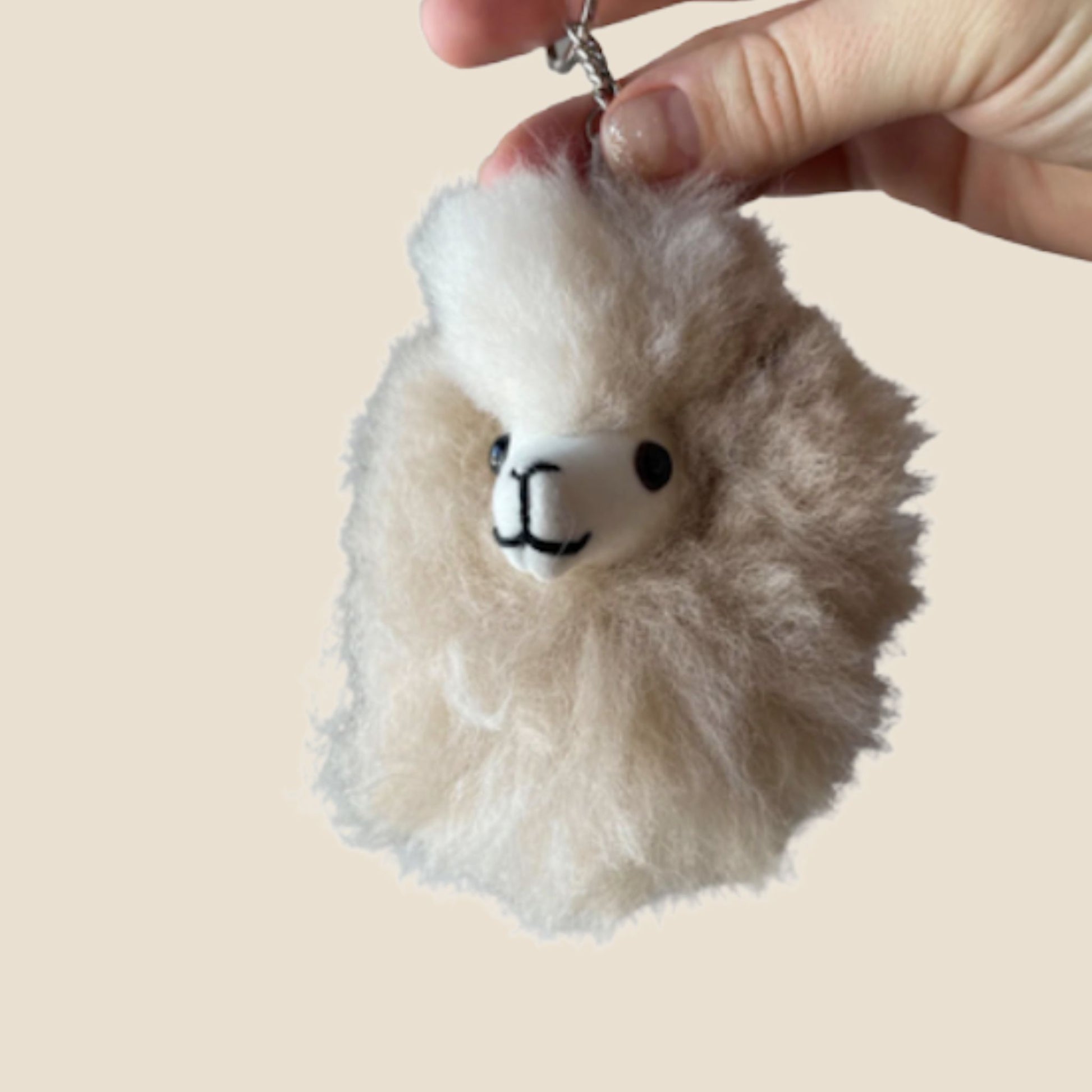 Fluffy keychain shaped like a alpaca held by a hand against a beige background