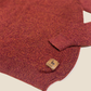 Close-up of a red knit sweater with a brand label on a beige background