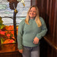Woman in a teal sweater standing in front of a stained glass window 