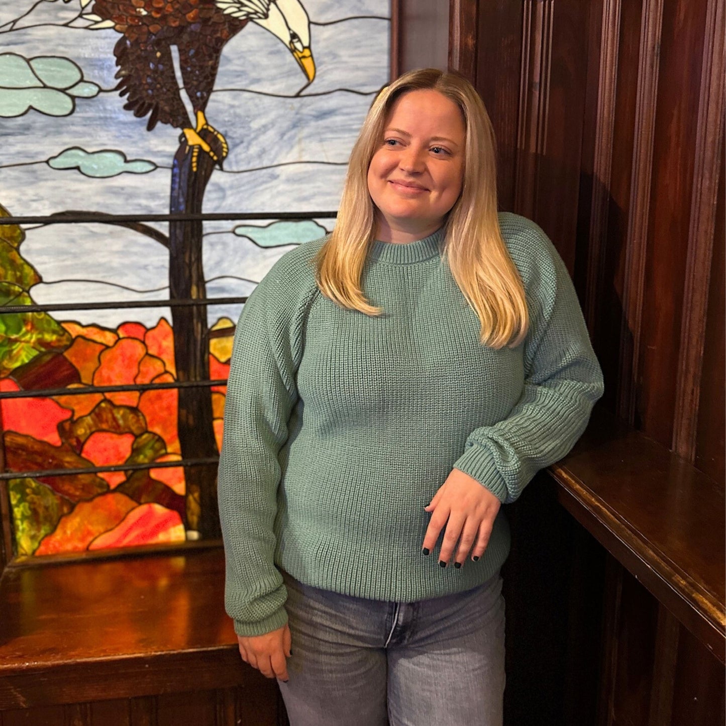 Woman in a teal sweater standing in front of a stained glass window 