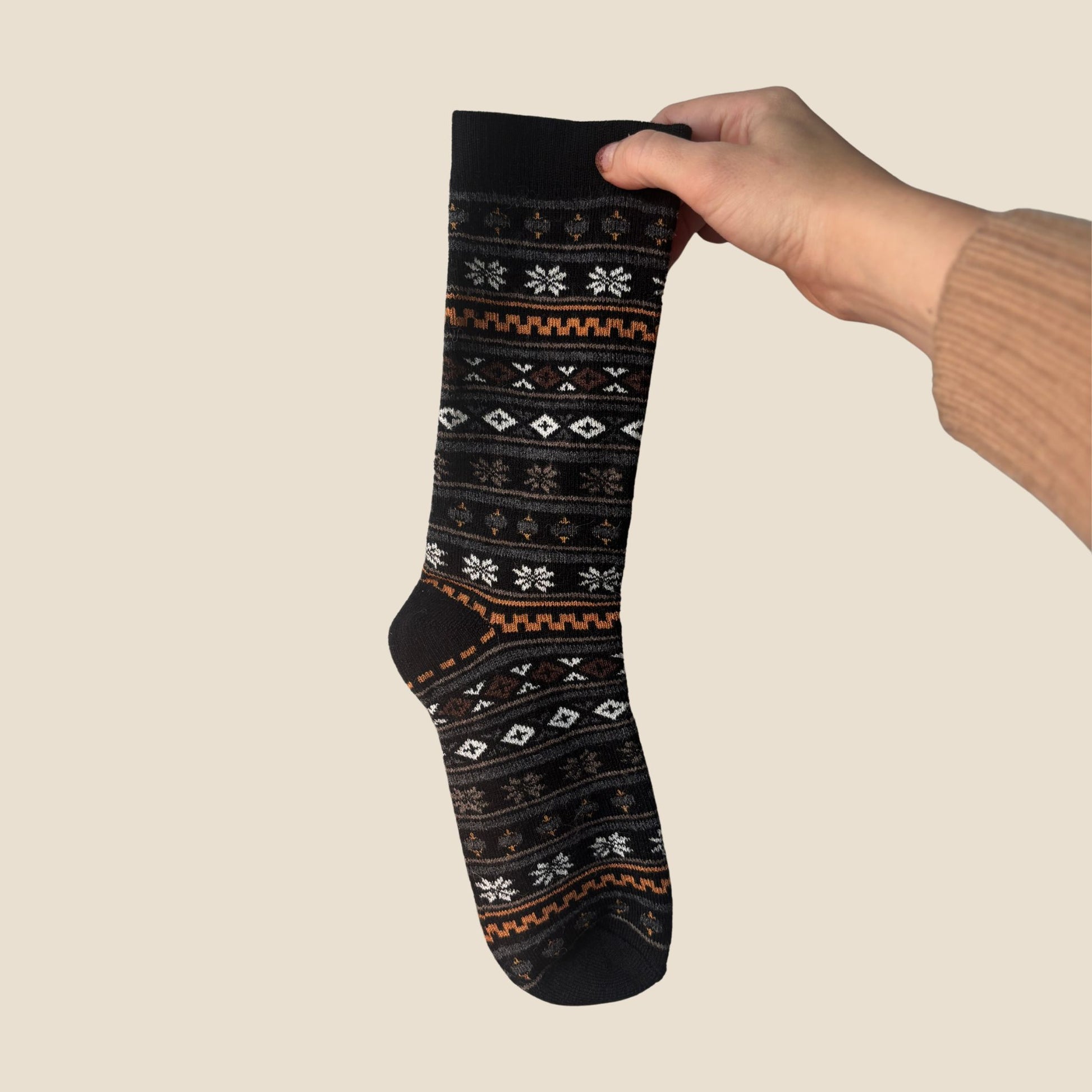 Hand holding a black sock with pattern against a beige background