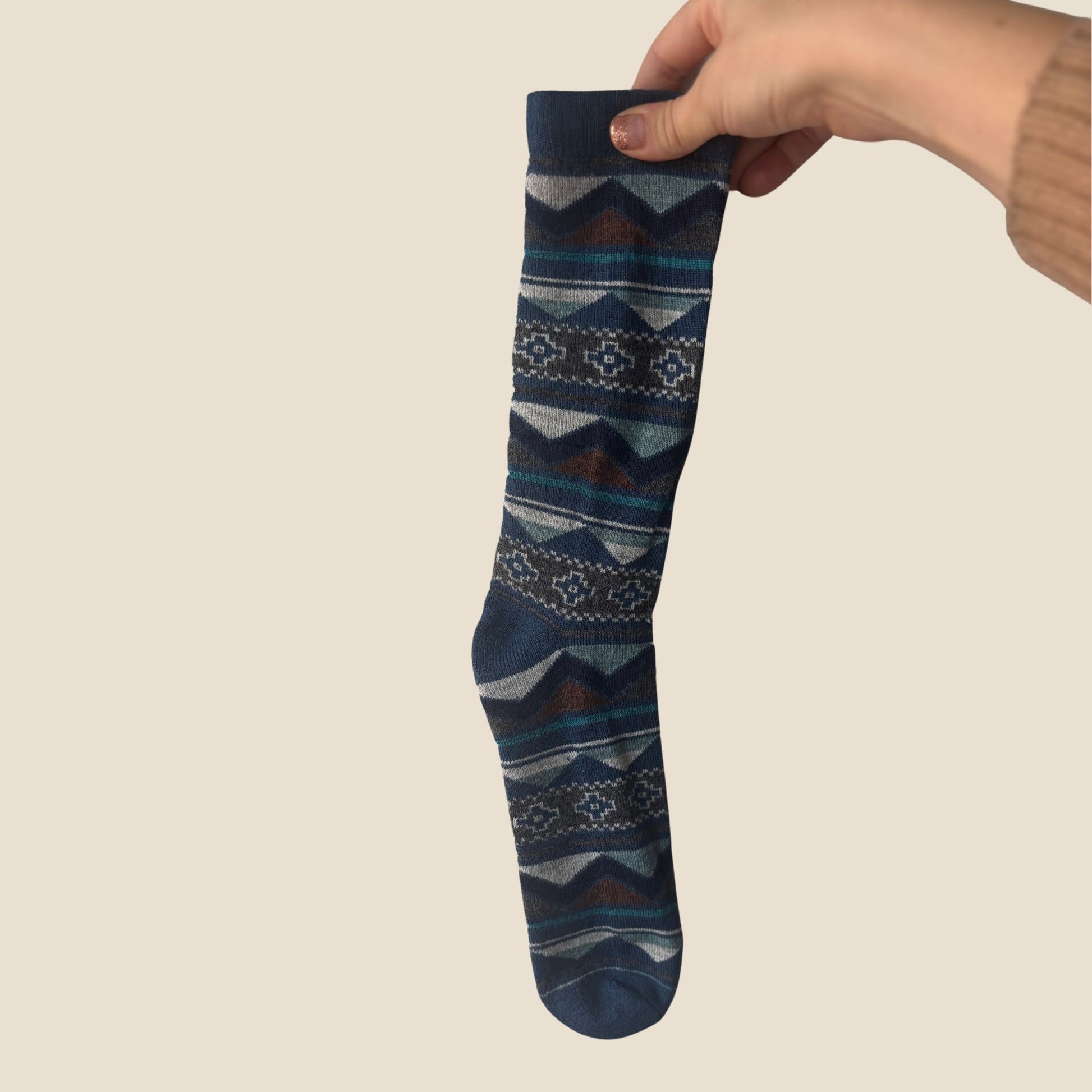 Hand holding a patterned sock against a beige background
