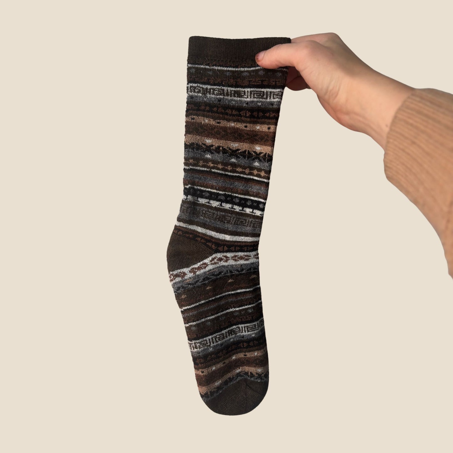 Hand holding a striped sock against a beige background