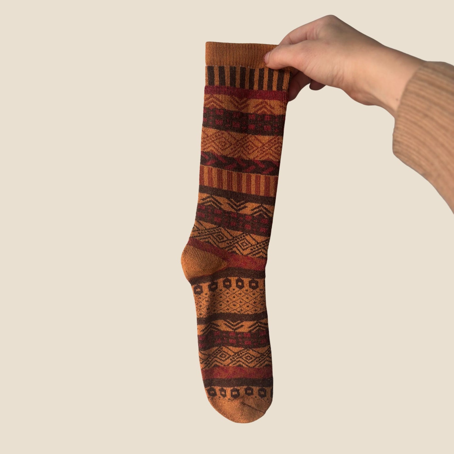 Hand holding a patterned sock against a beige background