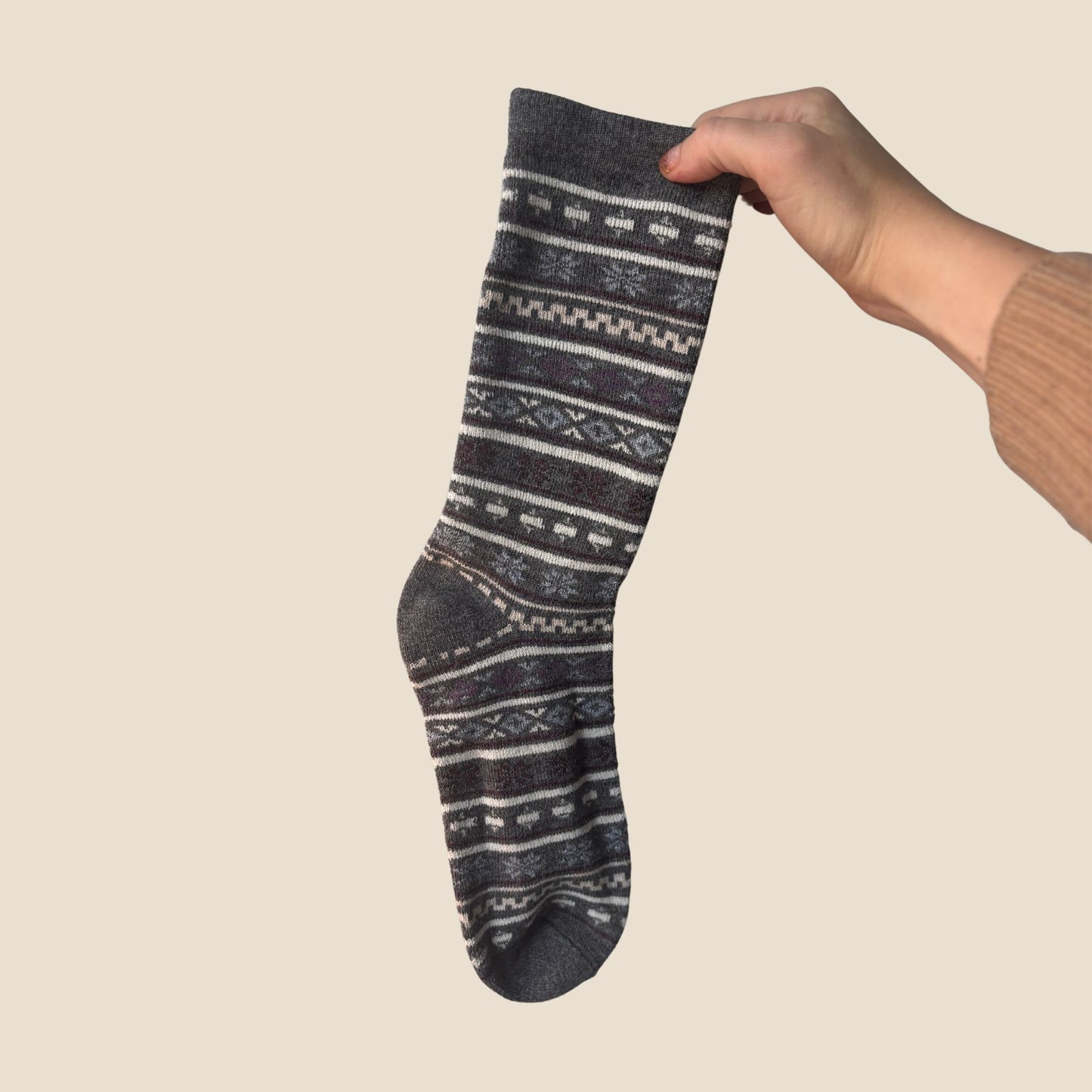 Hand holding a gray sock with white patterns against a beige background