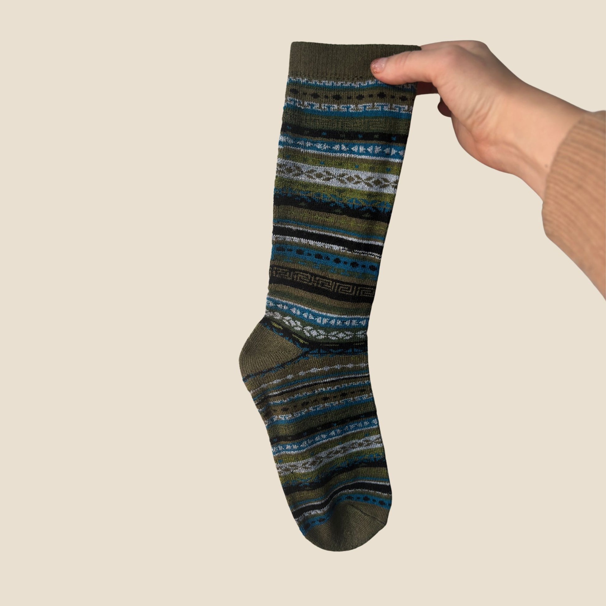 Hand holding a patterned sock against a beige background
