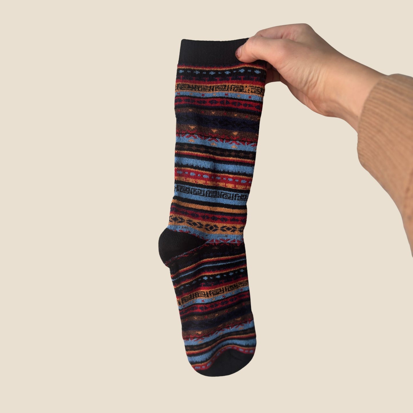 Colorful patterned sock held by a hand against a beige background