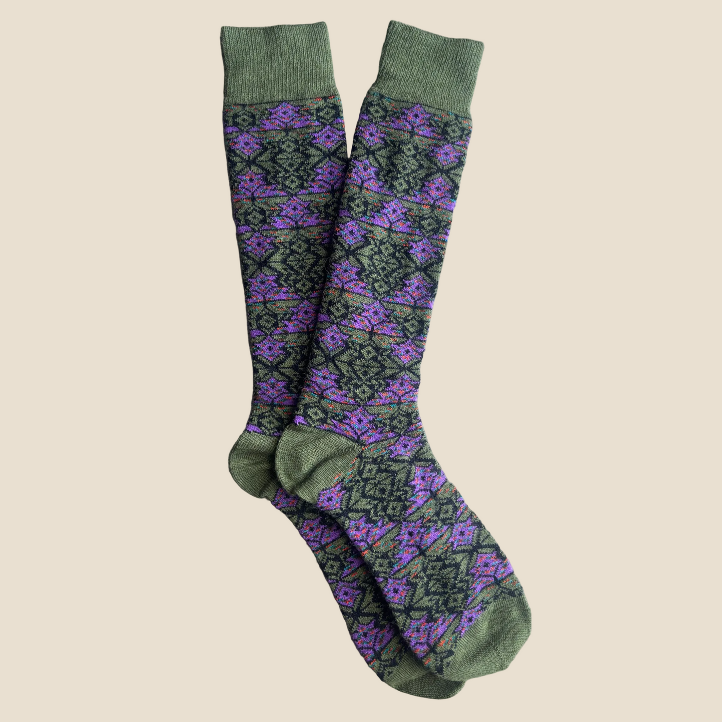 Pair of olive green knee-high socks with a purple geometric pattern on a wooden surface