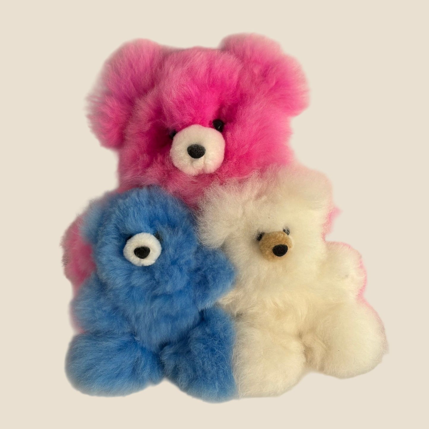 Three colorful teddy bears in pink, blue, and white on a beige background