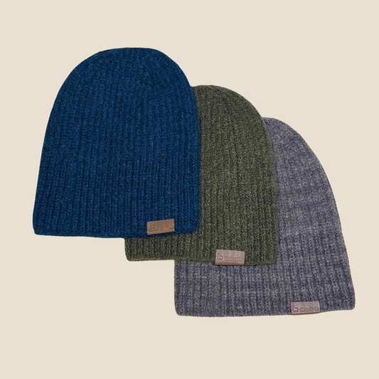 Three knit beanie hats in blue, green, and gray on a beige background