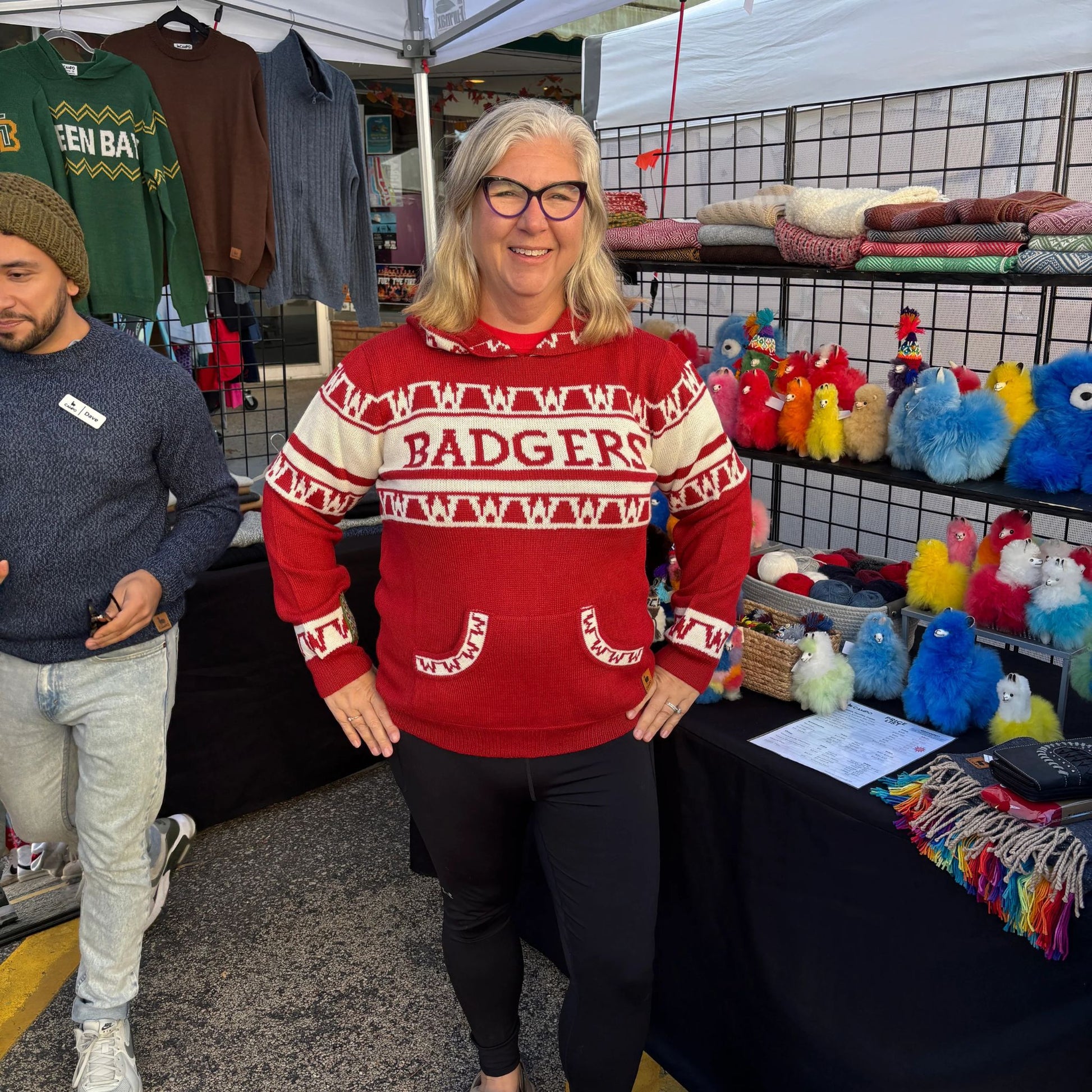 Person wearing a red 'Badgers' sweater at an outdoor market with various items on display.