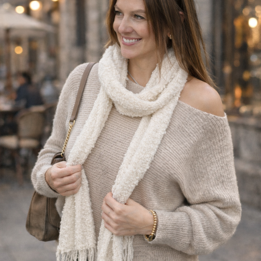 Woman wearing a beige sweater and white scarf in an outdoor setting