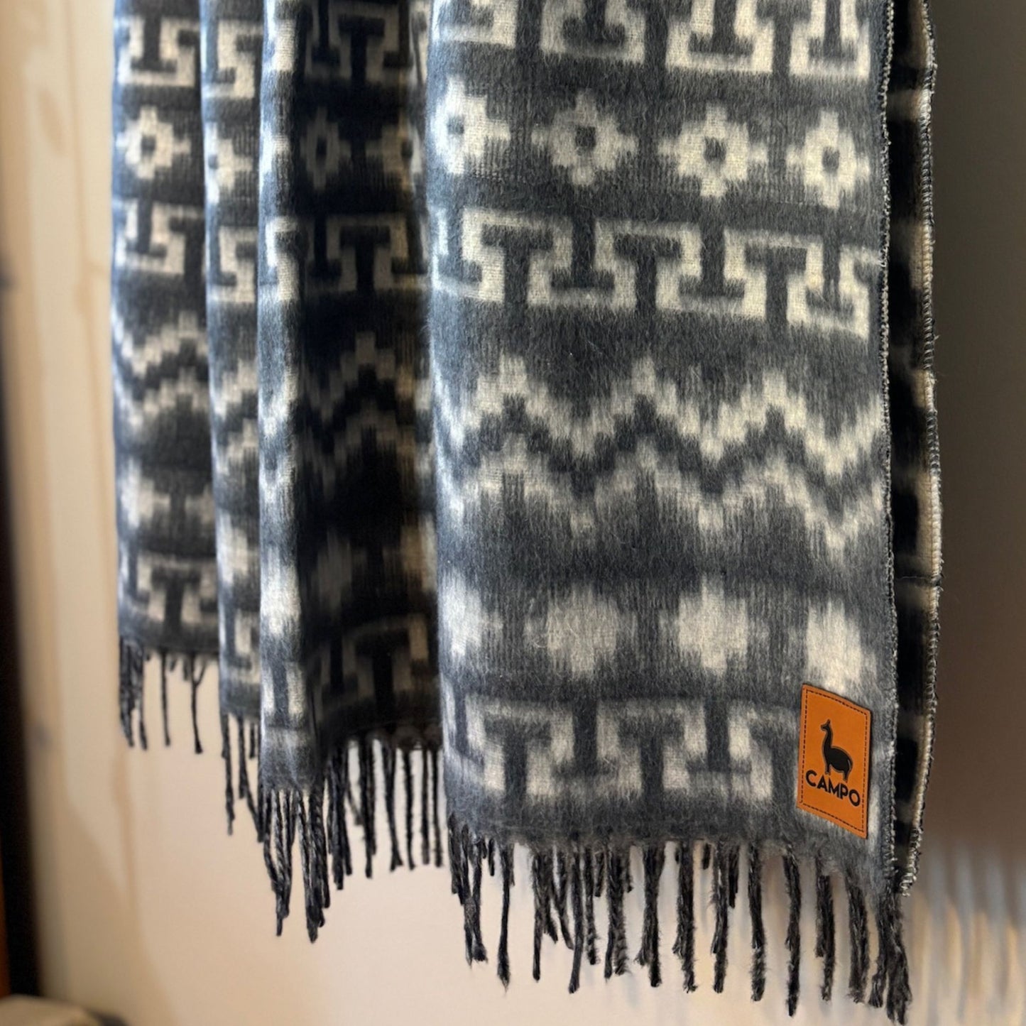Silver patterned scarf with fringes and a visible brand logo on a neutral background
