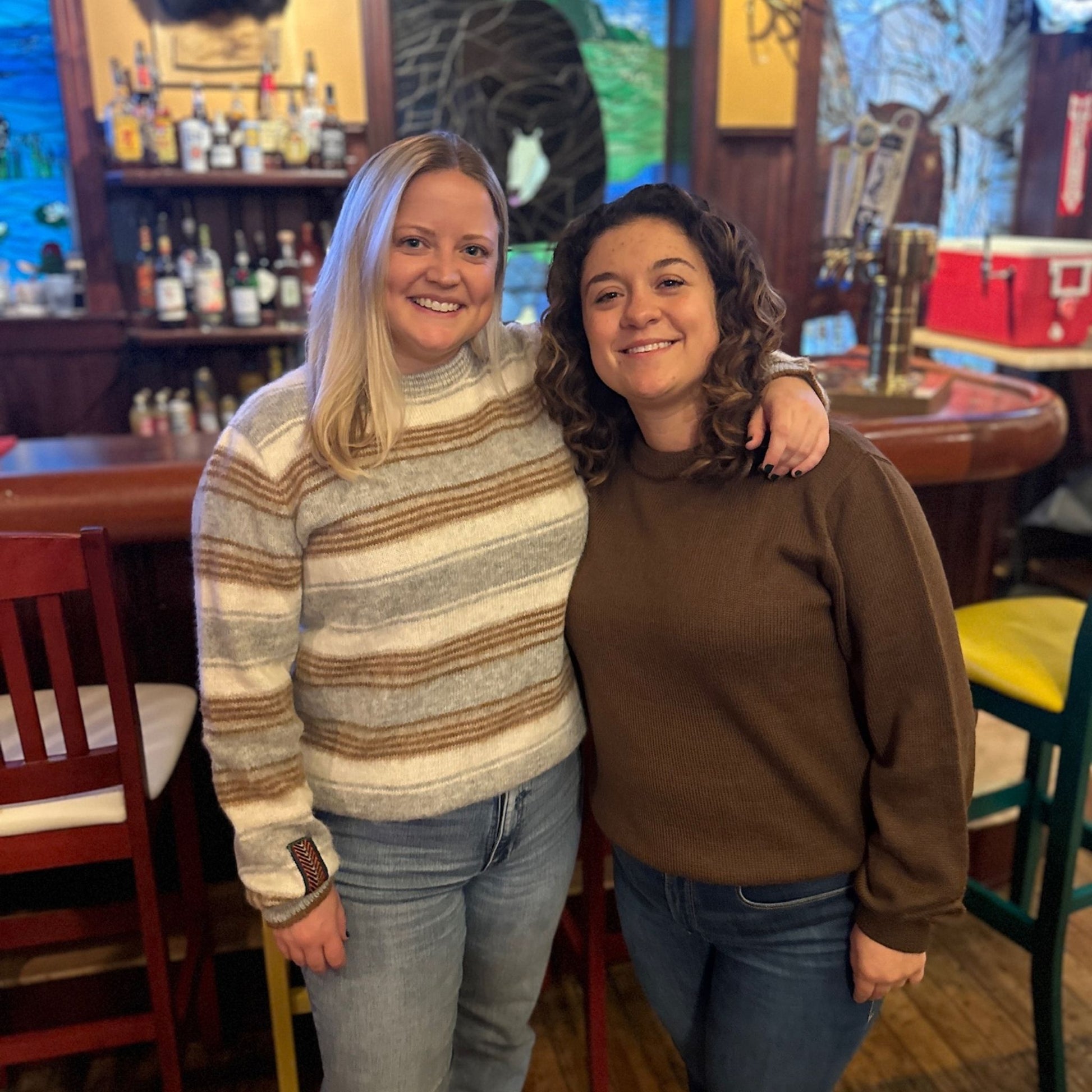 Two women posing together wearing striped alpaca and brown alpaca