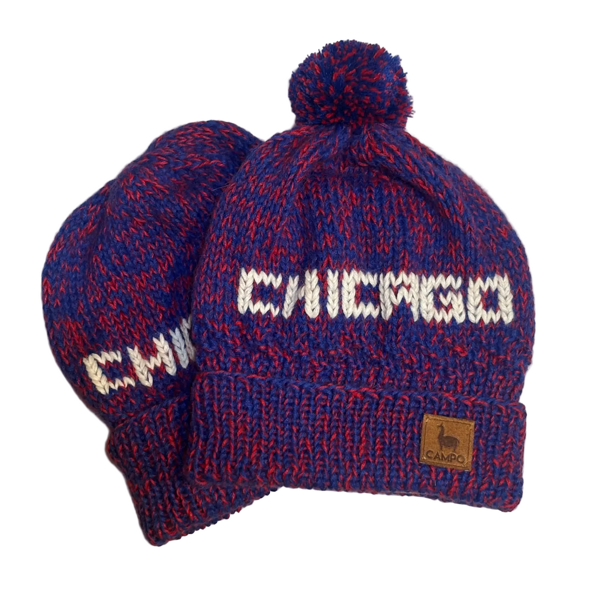 A pair of Chicago knit pom-pom beanies in a marled blue and red heathered pattern, featuring white knit lettering and a small brown brand patch.