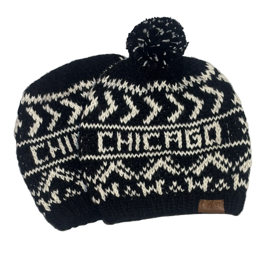A black and cream knit beanie hat with a pom-pom on top, featuring the word 'CHICAGO' knitted across the front and a small brown leather patch near the brim.