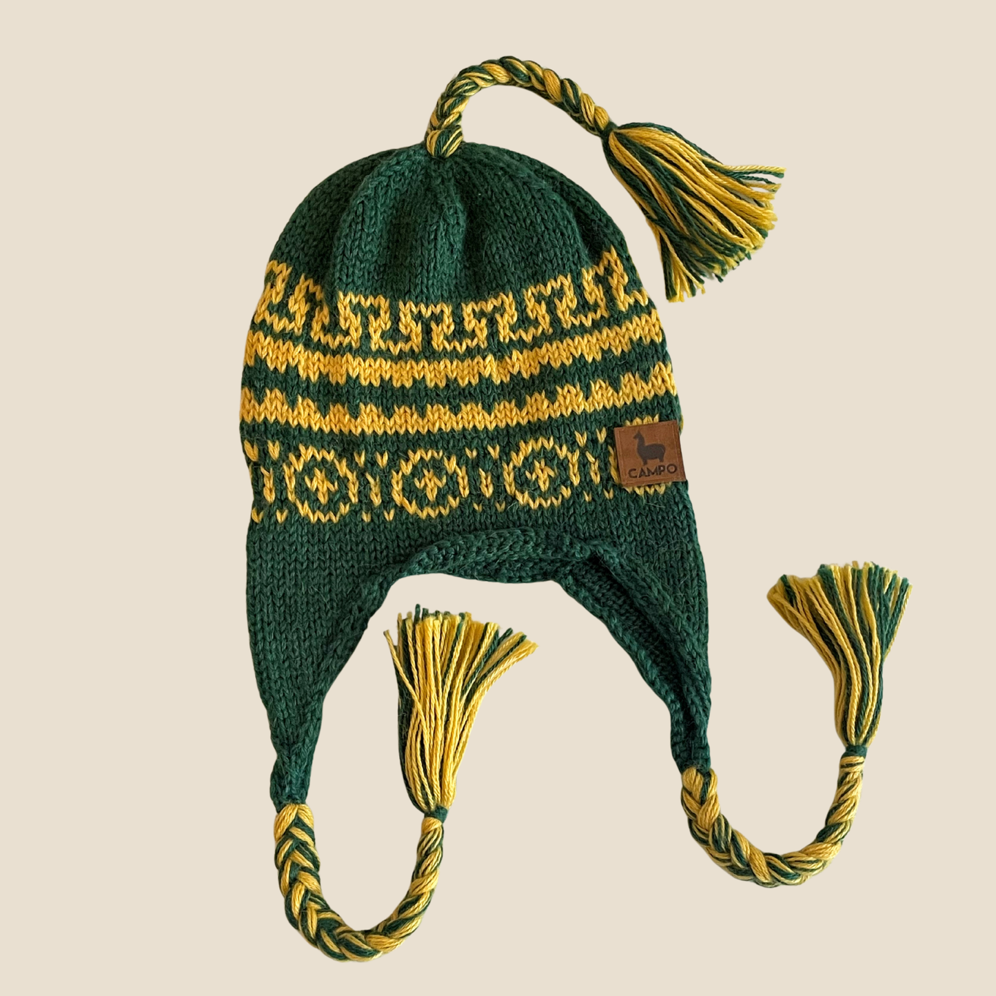 Green and yellow knitted hat with tassels on a beige background