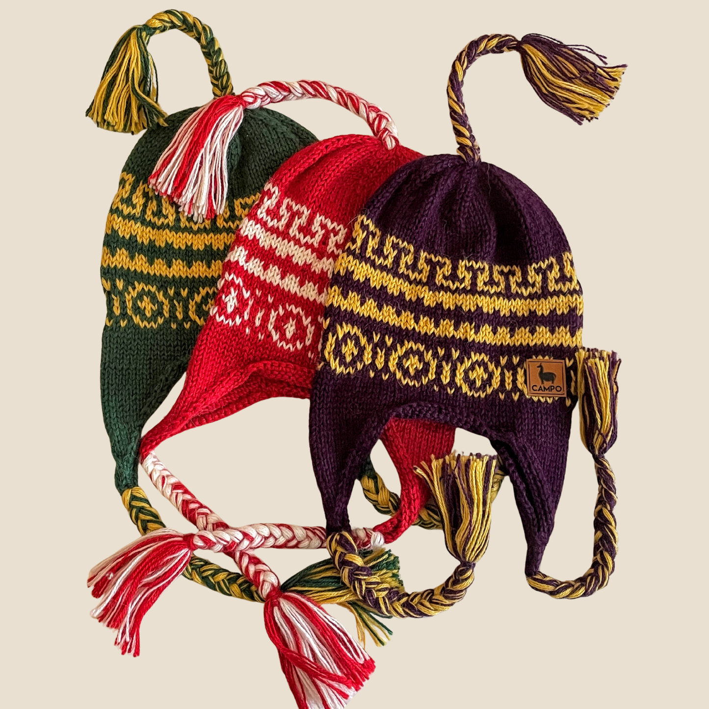 Three knitted hats with tassels on a beige background