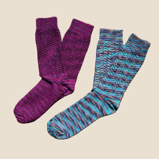 Two pairs of patterned socks, one purple and one multicolored, on a beige background.