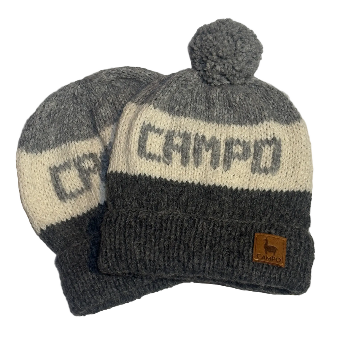 Two gray and cream knit beanie hats with pom-poms, one in front of the other. The front hat has 'CAMPO' knitted across the stripe, and a small tan leather patch with a llama logo is on the ribbed cuff.