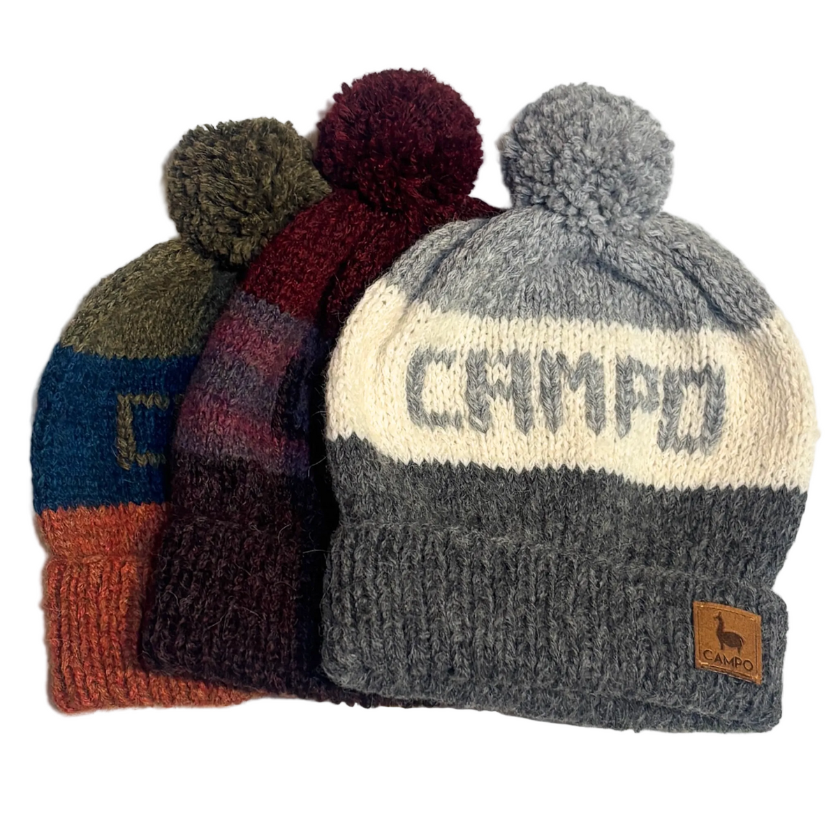 Four knitted pom-pom beanies arranged in a fan on a light background. The front hat is heather gray with a cream band reading CAMPO, dark gray cuff, and a small brown logo patch.