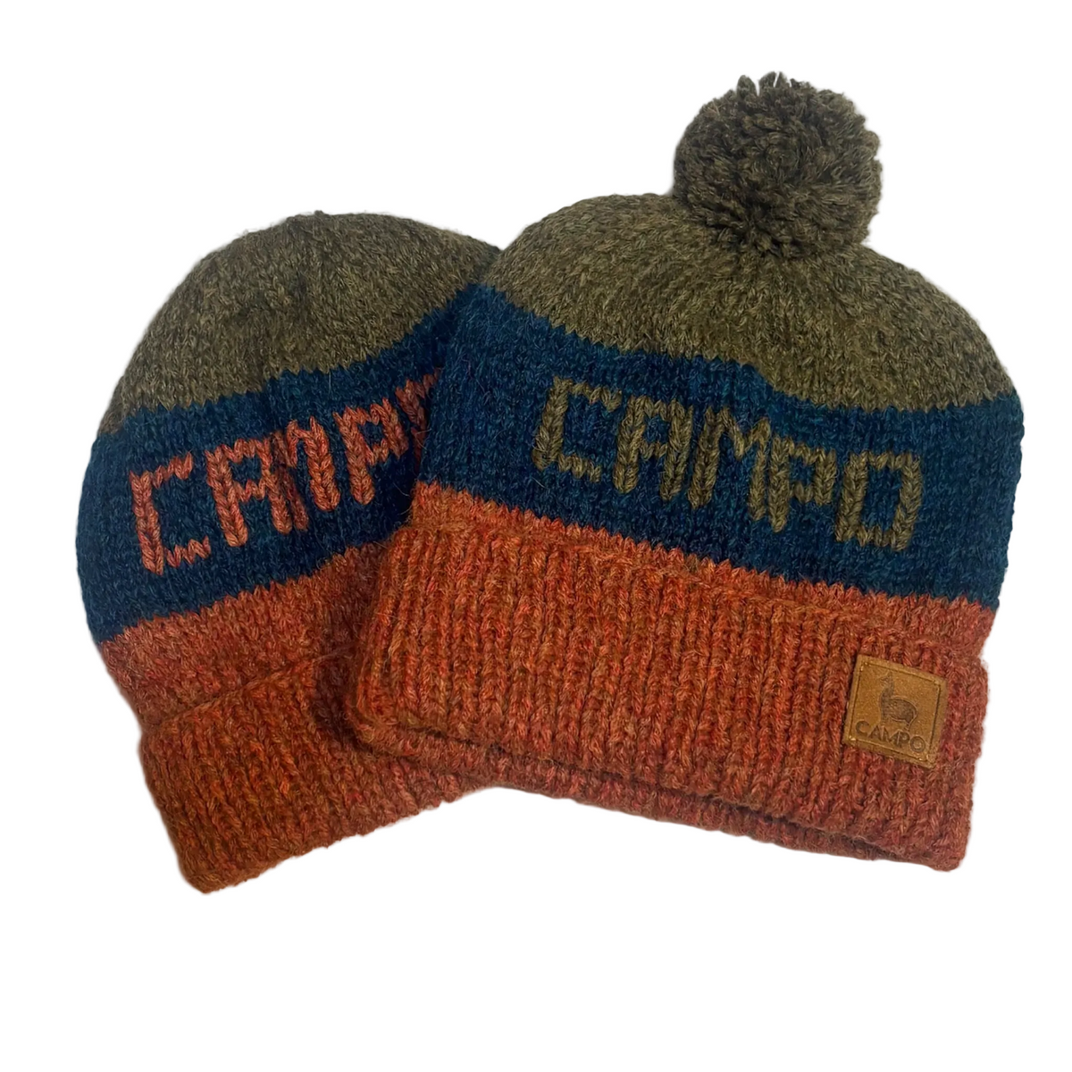 Two knit pom-pom beanies in a color-blocked design of olive green, navy blue, and rust orange. The front beanie features the word 'CAMPO' knitted across the middle, and a small tan leather patch on the cuff reads 'CAMP'.