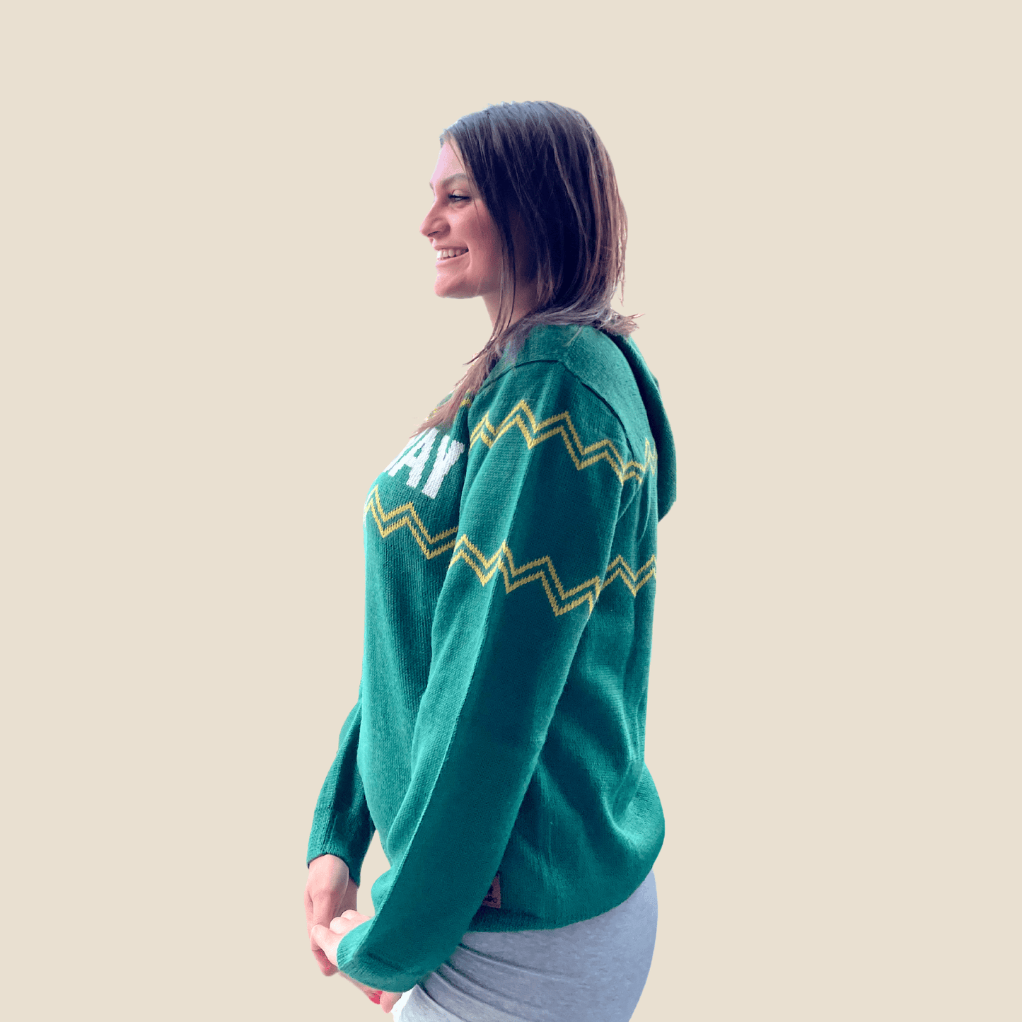 Woman wearing a green sweater with white text and yellow zigzag patterns on a beige background